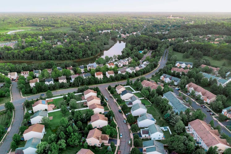 Flygfoto över ett lummigt villaområde med slingrande vägar, en damm och omgivande skog. Flygfoto över ett lummigt villaområde med slingrande vägar, en damm och omgivande skog.