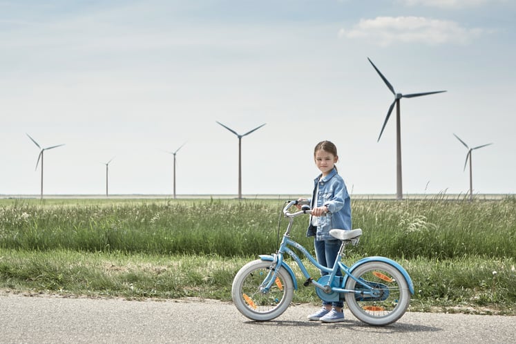 En flicka står med sin cykel framför en vindkraftspark