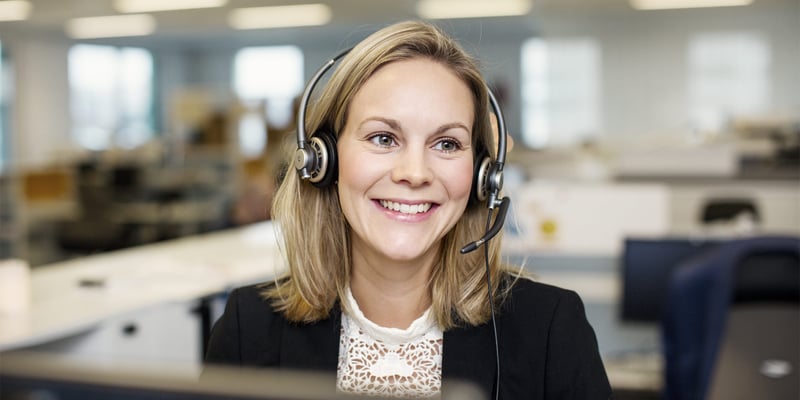 En kvinna med headset vid ett skrivbord i ett kontorslandskap.