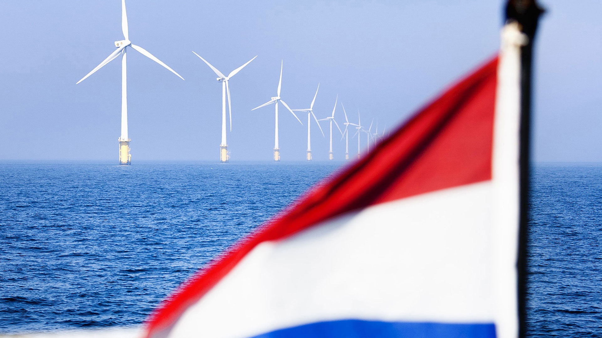 Den nederländska flaggan vajar framför en havsbaserad vindkraftspark