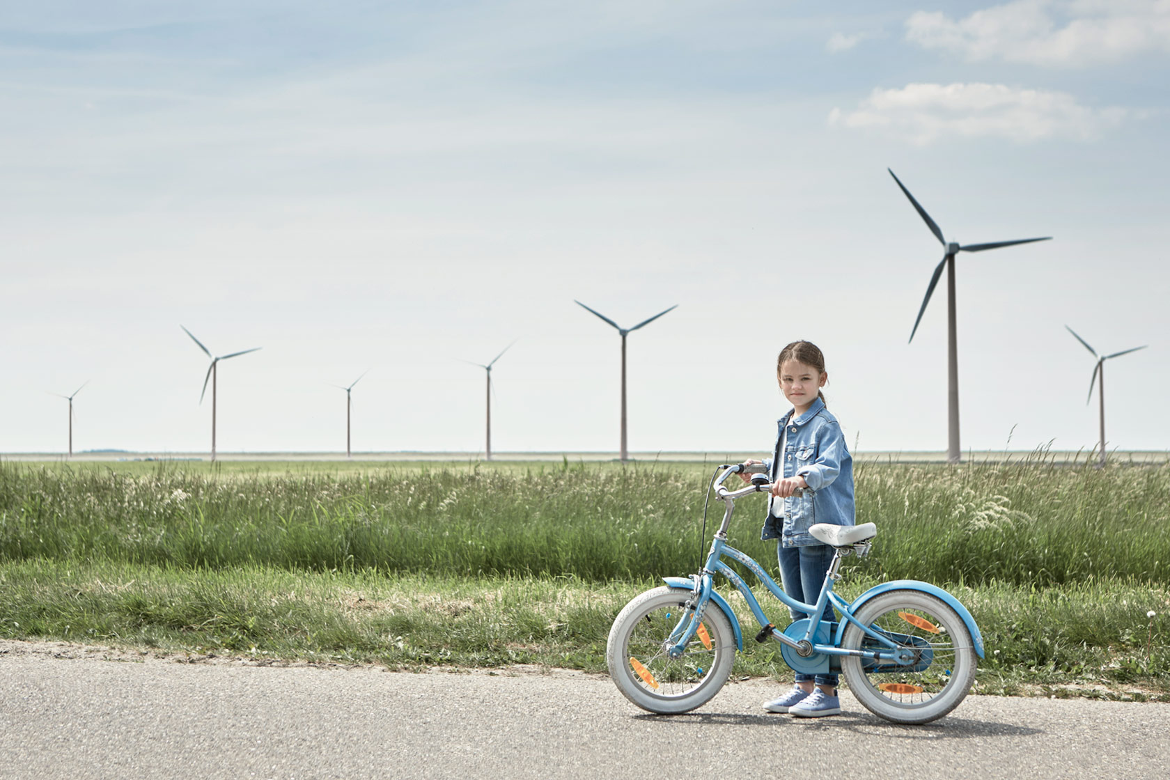 En flicka som står med sin cykel framför en vindkraftspark