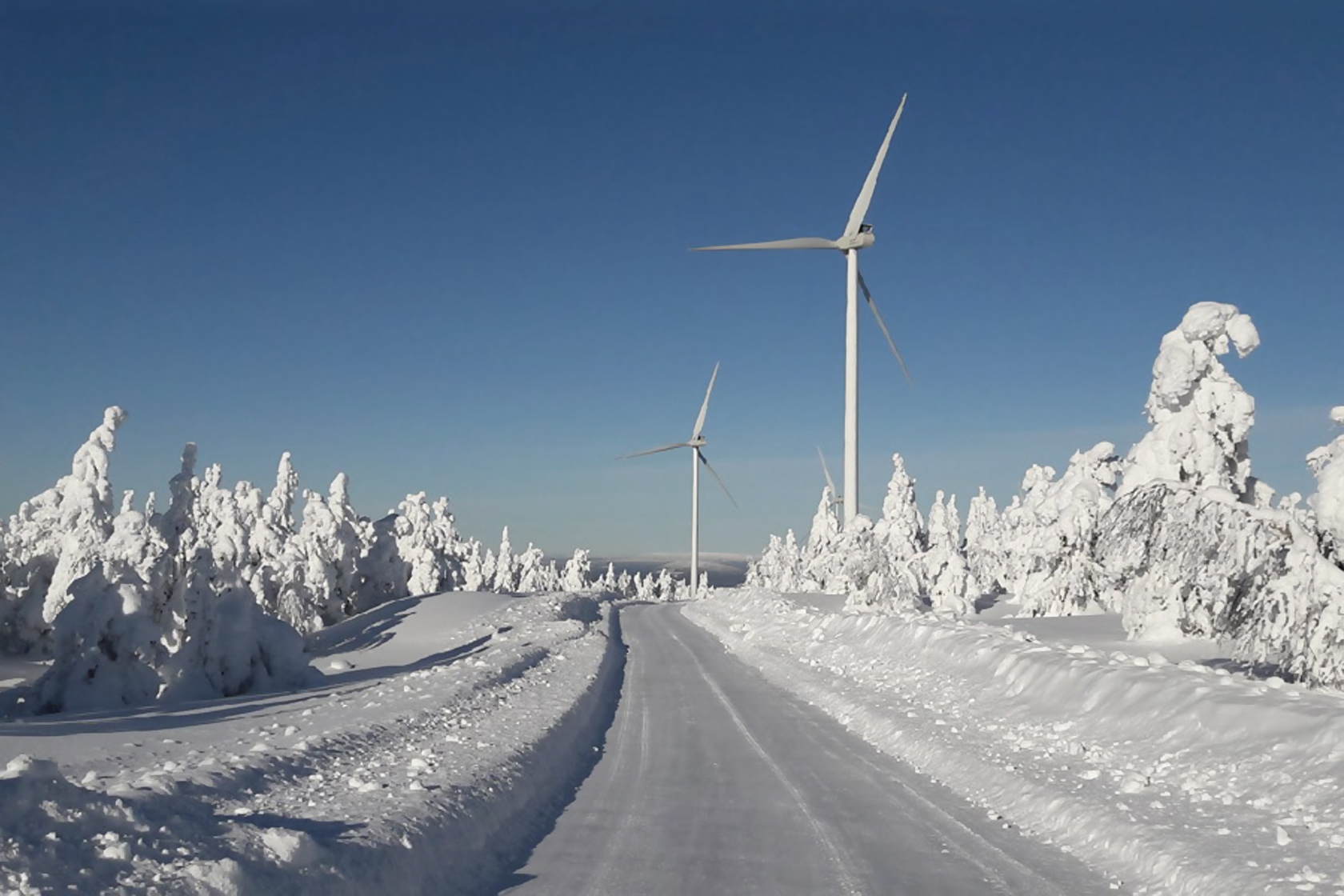 En väg och två vindkraftverk i snötäckt landskap Vindkraftverk i vinterlandskap