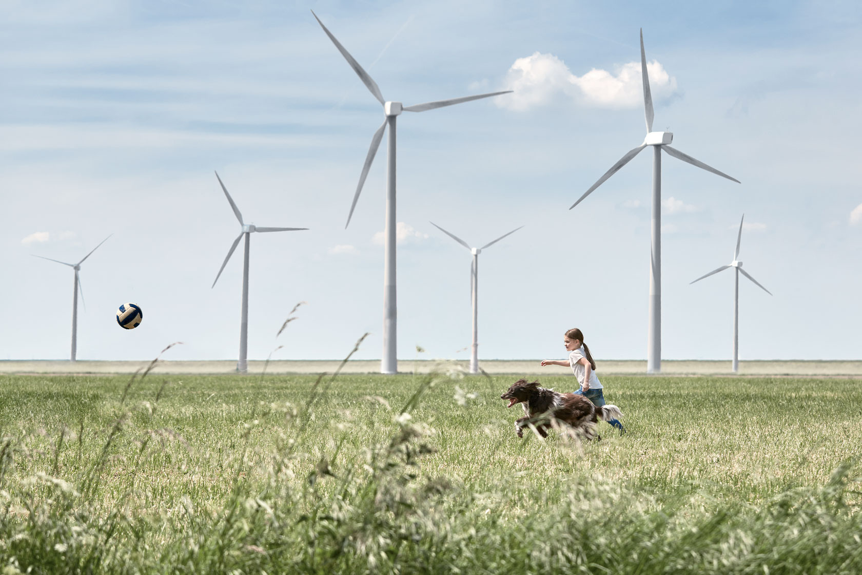 Ett barn och en hund jagar en boll framför vindkraftverk