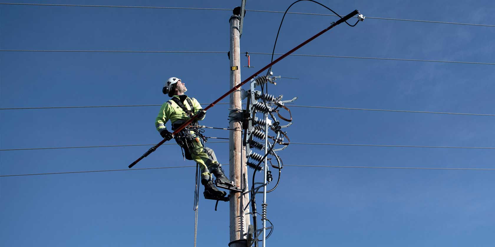 Employee in safety gear working on top of electricity pylon
