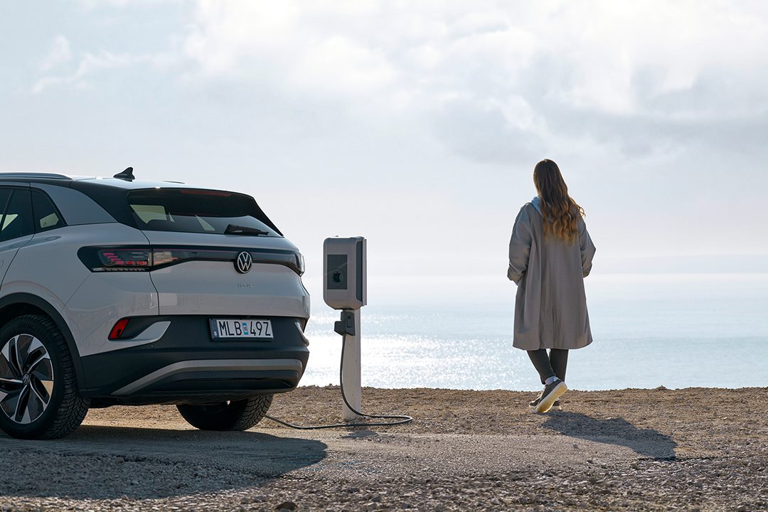 A woman standing by the sea while charging her electric car