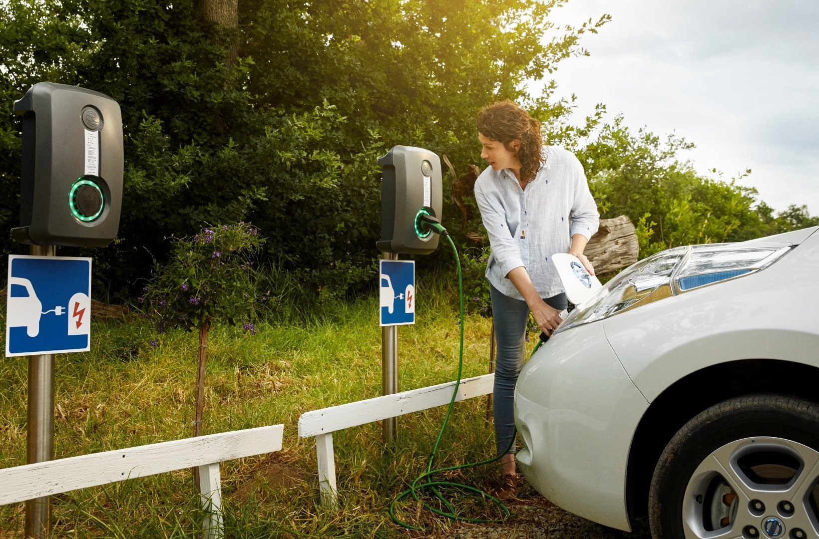 Woman using charging infrastructure to charge her electric vehicle Woman using charging infrastructure to charge her electric vehicle