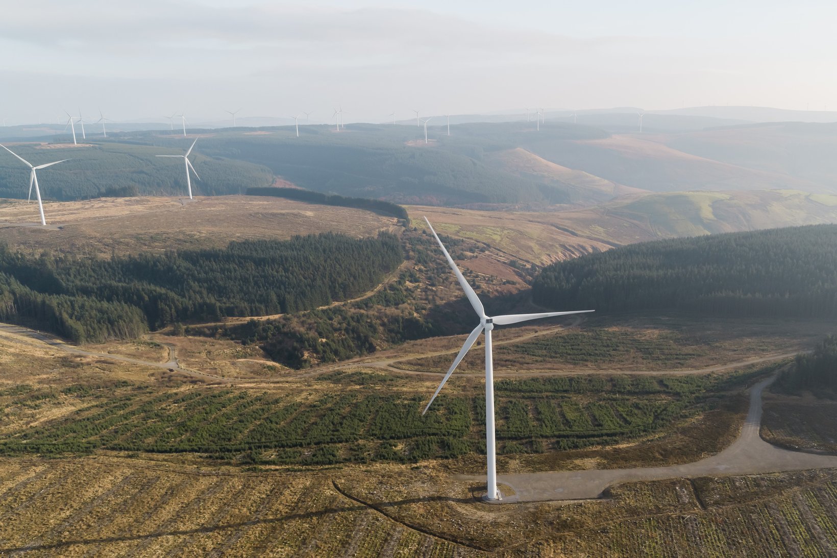 Aerial photo of a wind farm with several wind turbines located in a lush green landscape.