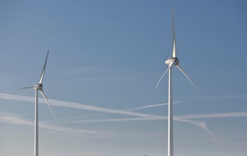 Image of two wind turbines, located in a field with blue skies above.