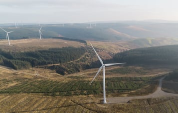 Aerial photo of a wind farm with several wind turbines located in a lush green landscape.