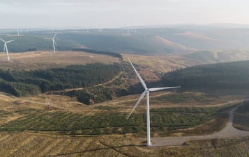 Aerial photo of a wind farm with several wind turbines located in a lush green landscape.