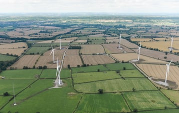 Areal photo of wind turbines in a green landscape.