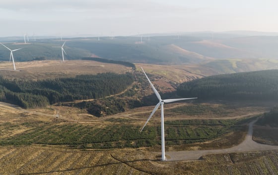 Aerial photo of a wind farm with several wind turbines located in a lush green landscape.
