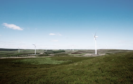 Photo of wind turbines located in a green landscape, with blue skies above.