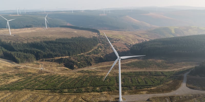 Aerial photo of a wind farm with several wind turbines located in a lush green landscape.