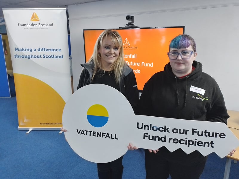 An image of two people holding a large cardboard sign that says 'Unlock Our Future Fund Recipient'