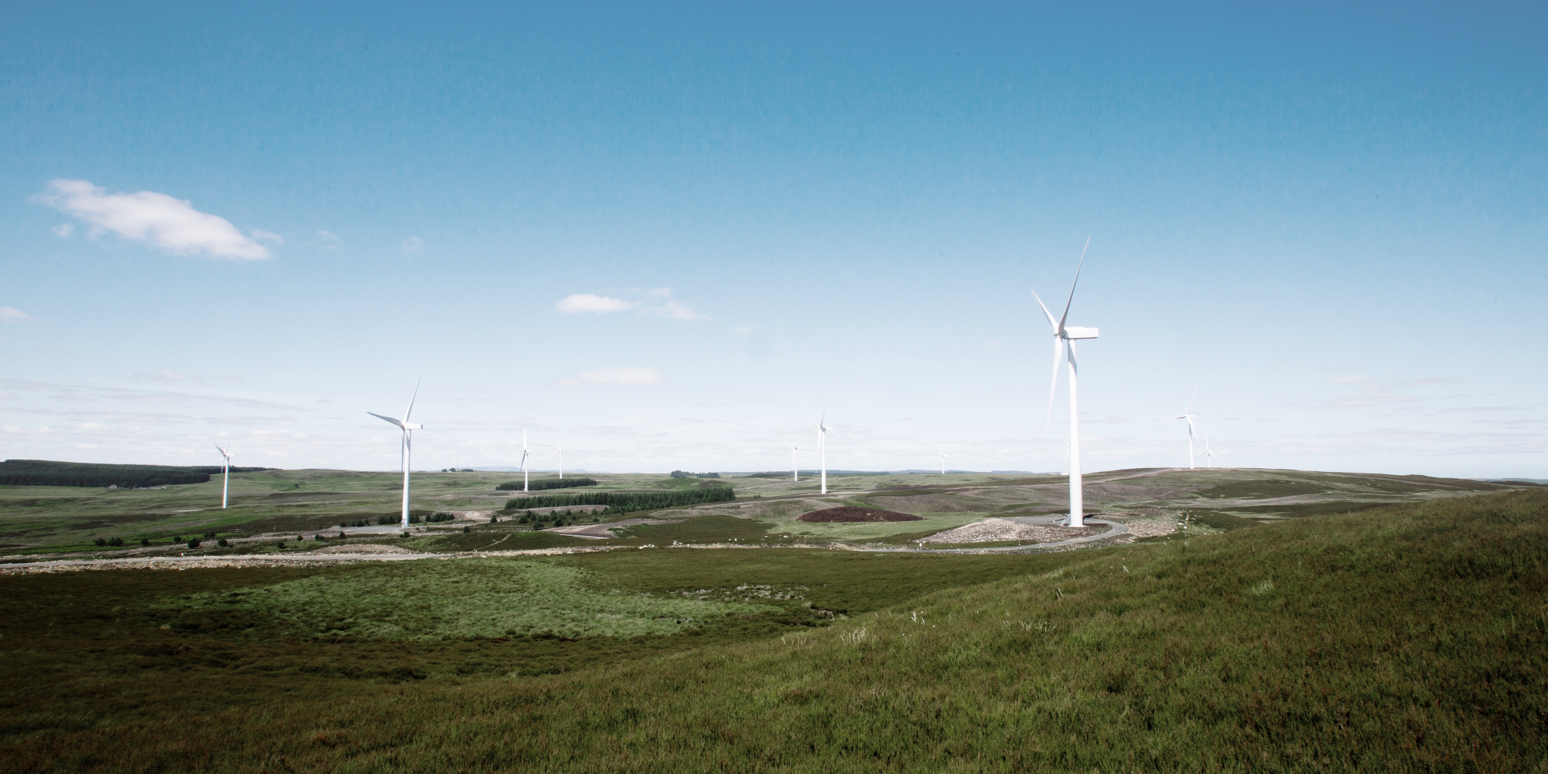Photo of wind turbines located in a green landscape, with blue skies above.