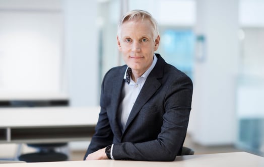 Sjur Jensen, Head of Business Area Markets, wearing in a dark business suit and sitting at a desk in a bright, modern office environment. Sjur Jensen, Head of Business Area Markets, wearing in a dark business suit and sitting at a desk in a bright, modern office environment.