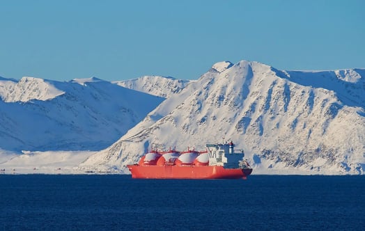 A large bright‑orange liquefied natural gas (LNG) tanker floats on deep blue water in front of a backdrop of tall, snow‑covered mountains under a clear blue sky. The rounded white storage domes on the ship stand out against the icy landscape. A large bright‑orange liquefied natural gas (LNG) tanker floats on deep blue water in front of a backdrop of tall, snow‑covered mountains under a clear blue sky. The rounded white storage domes on the ship stand out against the icy landscape.