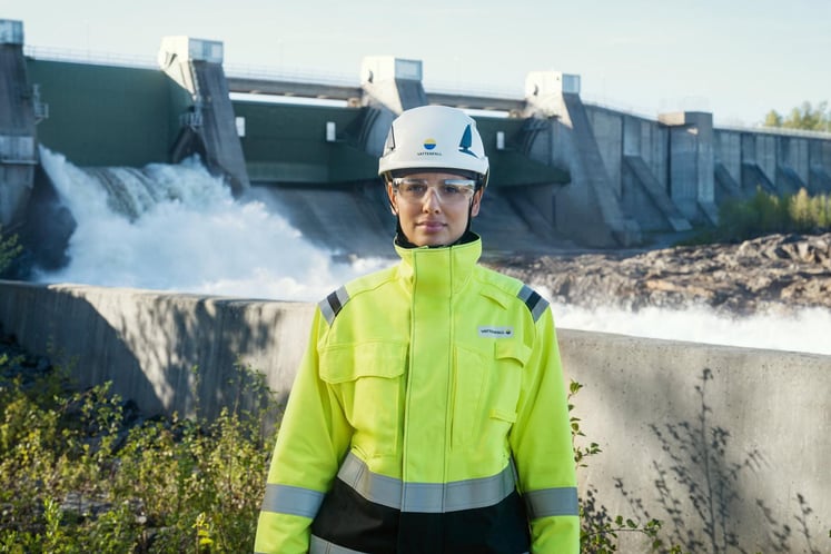 Woman in high-visibility safety clothing and helmet standing in front of a hydro power plant. Woman in high-visibility safety clothing and helmet standing in front of a hydro power plant.