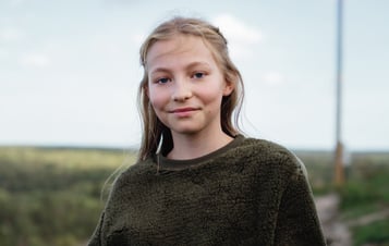 Flicka med grön tröja tittar in i kameran Flicka med grön tröja tittar in i kameran