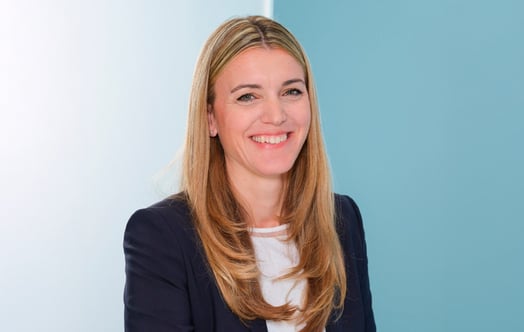 Porträtt av Sonja Müller-Dib, klädd i en marinblå kavaj och vit topp, framför en ljusblå bakgrund. Porträtt av Sonja Müller-Dib, klädd i en marinblå kavaj och vit topp, framför en ljusblå bakgrund.