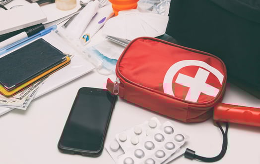 En samling nödvändiga saker för nödsituationer och resor utspridda på en vit yta, inklusive en röd första hjälpen-väska med ett vitt kors, blisterförpackningar med tabletter, en smartphone, pass som ligger på kontanter och olika små förnödenheter som pennor, tejp och medicinska artiklar. En samling nödvändiga saker för nödsituationer och resor utspridda på en vit yta, inklusive en röd första hjälpen-väska med ett vitt kors, blisterförpackningar med tabletter, en smartphone, pass som ligger på kontanter och olika små förnödenheter som pennor, tejp och medicinska artiklar.