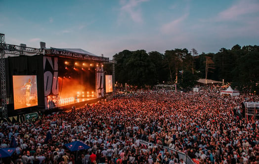 Tät publik framför en stor utomhusscen i en park i skymningen. Tät publik framför en stor utomhusscen i en park i skymningen.
